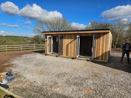 SIP build by FIS Finishes Small building with blue tarpaulin covering, set in a grassy area with trees nearby.