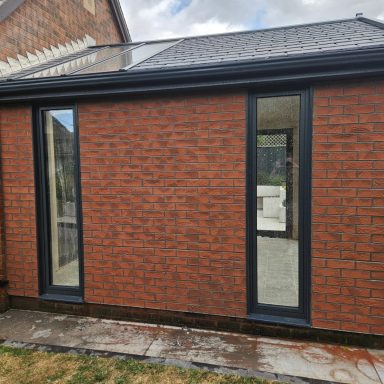 Brick mesh install by fisfinishes.com for 5 star windows Exterior view of a brick extension with large black-framed windows.