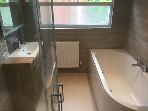 Modern bathroom featuring a shower, a bathtub, sink, and tiled walls.